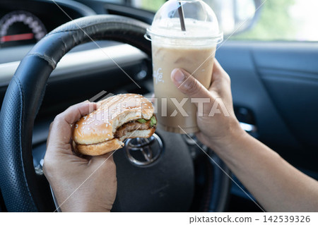 Bangkok, Thailand November, 2024 Asian woman driver hold and eat hamburger in car, dangerous and risk an accident. Bangkok, Thailand November, 2024 Asian woman driver hold and eat hamburger in car, dangerous and risk an accident. 142539326