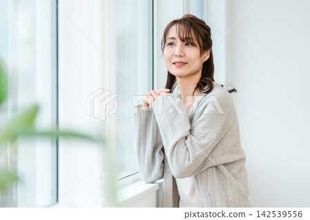 一位四五十歲的女性在明亮的窗邊微笑。這是她在自然環境中度過的一段寧靜時光。 142539556