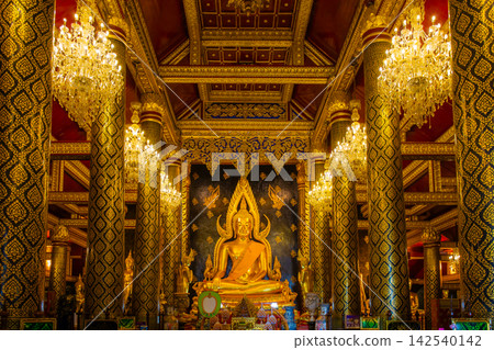 A large, beautiful golden Buddha statue adorned with intricate Thai-style pillars and decorative lanterns at Wat Phra Buddha Chinnarat in Phitsanulok, Thailand. A large, beautiful golden Buddha statue adorned with intricate Thai-style pillars and decorative lanterns at Wat Phra Buddha Chinnarat in Phitsanulok, Thailand. 142540142