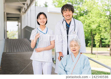 A doctor and nurse escorting a senior inpatient in a wheelchair in a hospital corridor. A doctor and nurse escorting a senior inpatient in a wheelchair in a hospital corridor. 142540586