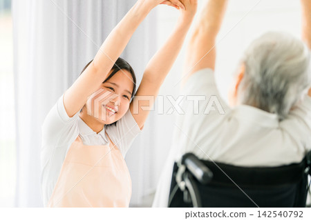 一位微笑的護理員幫助坐在輪椅上的老婦人做伸展運動。 一位微笑的護理員幫助坐在輪椅上的老婦人做伸展運動。 142540792