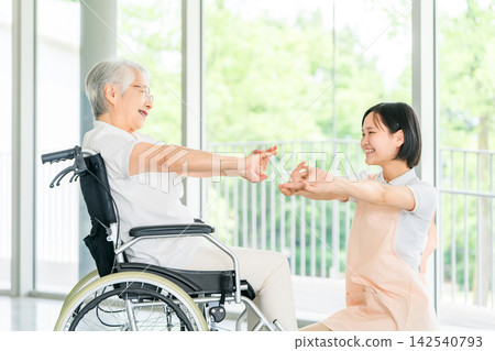 一位微笑的護理員幫助坐在輪椅上的老婦人做伸展運動。 一位微笑的護理員幫助坐在輪椅上的老婦人做伸展運動。 142540793