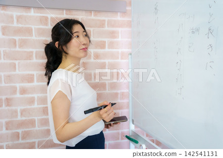 一位三十多歲的日本女性在訓練室的白板上寫字時，轉過身來微笑。 142541131