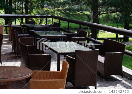 Outdoor wicker furniture set with table by a stream in a lush garden. Outdoor wicker furniture set with table by a stream in a lush garden. 142542753