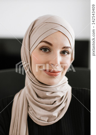 A portrait of a young woman wearing a beige hijab and a black top, looking directly at the camera with a gentle smile A portrait of a young woman wearing a beige hijab and a black top, looking directly at the camera with a gentle smile 142543409