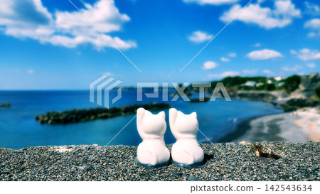 沙灘上,一隻白色的招手貓雕像凝視著蔚藍的大海和天空。 沙灘上,一隻白色的招手貓雕像凝視著蔚藍的大海和天空。 142543634