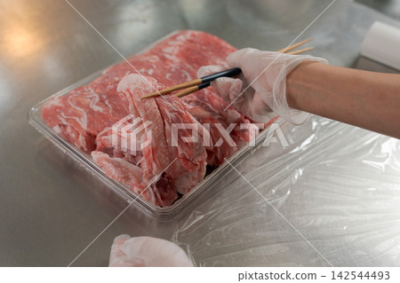 A woman's hands dividing a large quantity of meat into smaller portions. A woman's hands dividing a large quantity of meat into smaller portions. 142544493