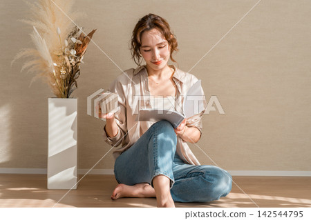 Women in their 40s and 50s relax barefoot in a room bathed in sunlight, enjoying coffee and reading. Women in their 40s and 50s relax barefoot in a room bathed in sunlight, enjoying coffee and reading. 142544795