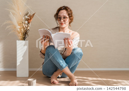A woman enjoying a book while sipping coffee in a warm, sunlit room. A woman enjoying a book while sipping coffee in a warm, sunlit room. 142544798