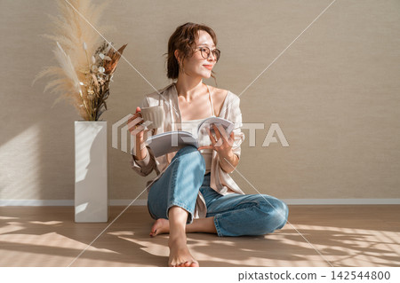 A woman enjoying reading and coffee barefoot in a warm, sunlit room. A woman enjoying reading and coffee barefoot in a warm, sunlit room. 142544800