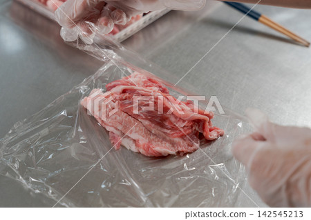 A woman's hands dividing a large quantity of meat into smaller portions. A woman's hands dividing a large quantity of meat into smaller portions. 142545213
