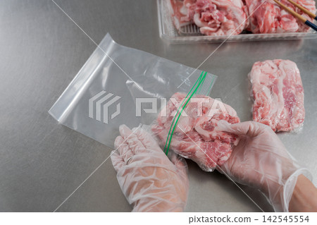 A woman's hands dividing a large quantity of pork into smaller portions. A woman's hands dividing a large quantity of pork into smaller portions. 142545554