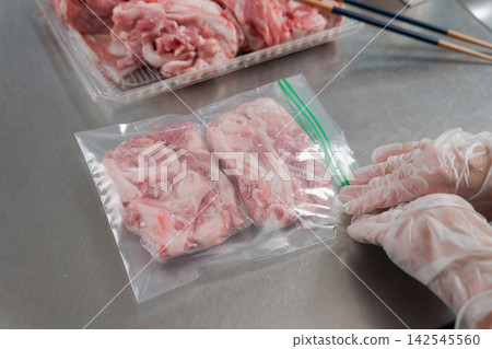 A woman's hands dividing a large quantity of pork into smaller portions. A woman's hands dividing a large quantity of pork into smaller portions. 142545560