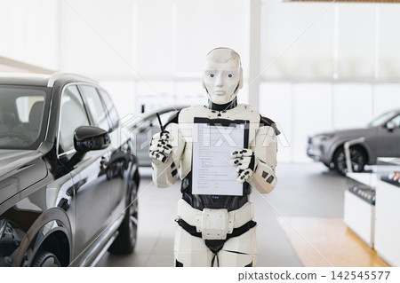 A humanoid robot stands in a car dealership holding a vehicle purchase agreement and pen, ready to assist customers with sales A humanoid robot stands in a car dealership holding a vehicle purchase agreement and pen, ready to assist customers with sales 142545577