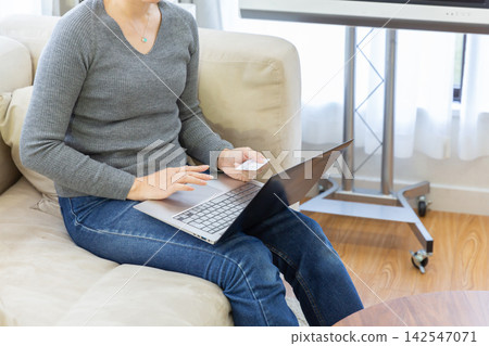 A woman using a credit card to make an online payment on her computer. A woman using a credit card to make an online payment on her computer. 142547071