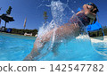 Happy young girl splashing in a swimming pool from a slide 142547782