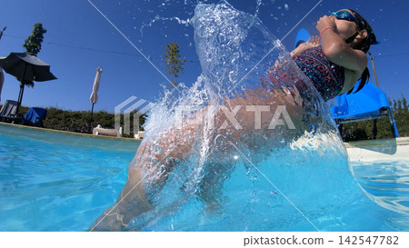 Happy young girl splashing in a swimming pool from a slide Happy young girl splashing in a swimming pool from a slide 142547782