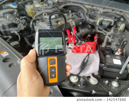 Close-up of Technician Testing AGM Car Battery Voltage and Condition with Digital Tester Tool in Garage. 142547880