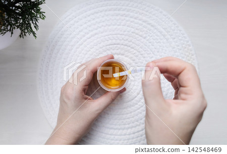 Person dipping a reagent test strip into a urine specimen container for medical analysis. Practical home diagnostic test checking health parameters and biomarkers. Person dipping a reagent test strip into a urine specimen container for medical analysis. Practical home diagnostic test checking health parameters and biomarkers. 142548469