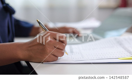 Businesswoman hand holding pen and writing on paper document at office desk. Female accountant signing agreement contract and checking financial report with laptop computer. Businesswoman hand holding pen and writing on paper document at office desk. Female accountant signing agreement contract and checking financial report with laptop computer. 142548587