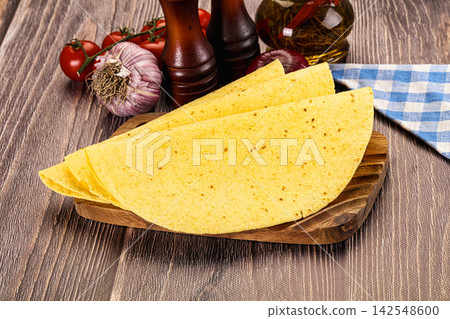 Yellow corn tortillas on wooden cutting board with garlic tomatoes and spice jars Yellow corn tortillas on wooden cutting board with garlic tomatoes and spice jars 142548600