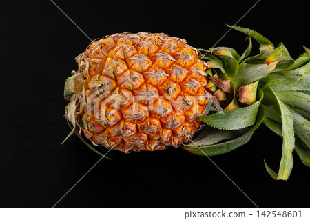 Ripe pineapple with green crown on black background Ripe pineapple with green crown on black background 142548601