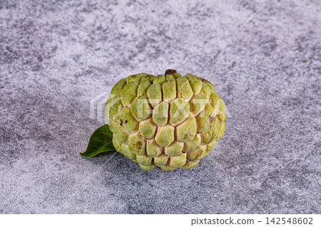 Fresh green custard apple with leaf on textured gray surface Fresh green custard apple with leaf on textured gray surface 142548602