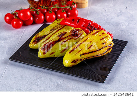 Grilled yellow and red peppers on black plate with cherry tomatoes background 142548641