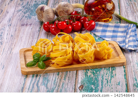 Fresh uncooked pasta nests with cherry tomatoes, garlic, basil and olive oil on rustic wooden board 142548645