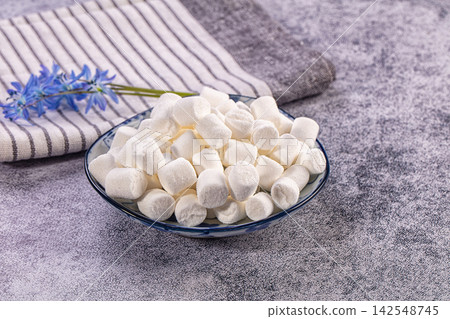White marshmallows in blue patterned bowl with striped cloth and blue flower 142548745