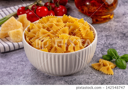 Uncooked farfalle pasta in white bowl with cherry tomatoes, basil, and parmesan cheese on gray surface Uncooked farfalle pasta in white bowl with cherry tomatoes, basil, and parmesan cheese on gray surface 142548747