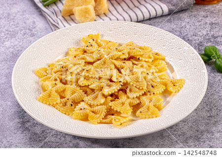 Cooked farfalle pasta with black pepper on textured white plate 142548748