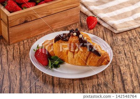Fresh croissant with chocolate drizzle and strawberries on rustic wood table Fresh croissant with chocolate drizzle and strawberries on rustic wood table 142548764
