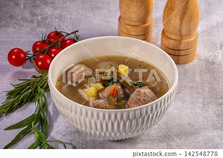 Hearty meatball soup with vegetables in white textured bowl, cherry tomatoes and rosemary on gray background Hearty meatball soup with vegetables in white textured bowl, cherry tomatoes and rosemary on gray background 142548778