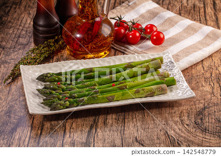 Fresh green asparagus spears on white ceramic plate with cherry tomatoes and olive oil 142548779