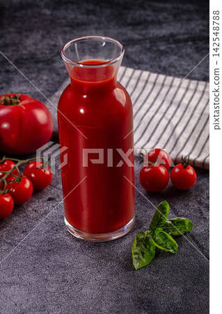 Glass carafe of fresh tomato juice with whole tomatoes and basil on dark textured surface Glass carafe of fresh tomato juice with whole tomatoes and basil on dark textured surface 142548788