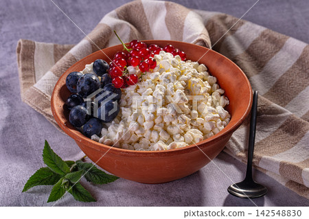Cottage cheese with blueberries and red currants in terracotta bowl on striped cloth Cottage cheese with blueberries and red currants in terracotta bowl on striped cloth 142548830