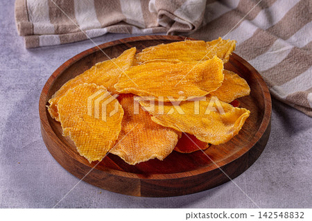Dry mango slices on wooden plate with striped cloth background Dry mango slices on wooden plate with striped cloth background 142548832