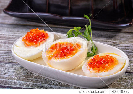 Boiled egg halves topped with red caviar on white plate with green garnish Boiled egg halves topped with red caviar on white plate with green garnish 142548852