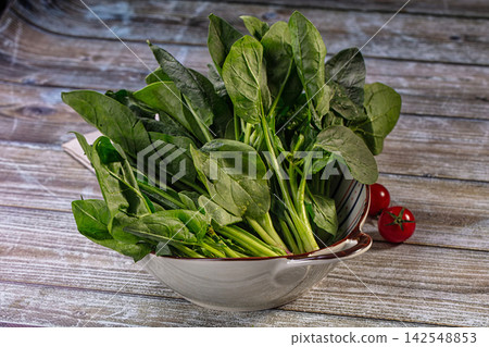 Fresh spinach leaves in ceramic bowl with cherry tomatoes on rustic wooden table Fresh spinach leaves in ceramic bowl with cherry tomatoes on rustic wooden table 142548853