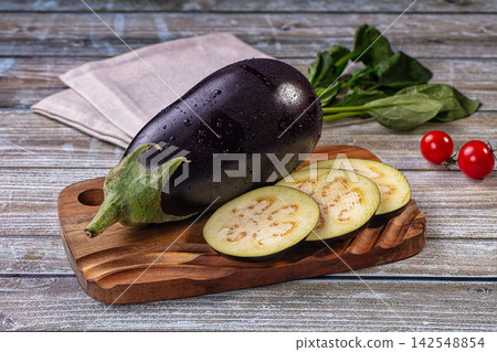 Fresh eggplant whole and sliced on wooden cutting board with spinach and cherry tomatoes Fresh eggplant whole and sliced on wooden cutting board with spinach and cherry tomatoes 142548854