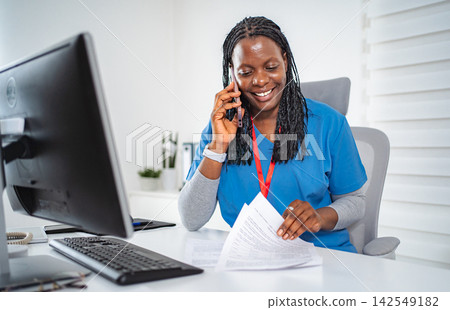 Female nurse communicating on phone while working in office Female nurse communicating on phone while working in office 142549182