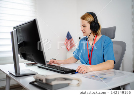 Nurse wearing headset operating computer for telehealth consultation Nurse wearing headset operating computer for telehealth consultation 142549196