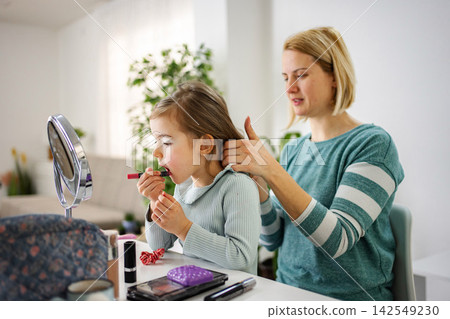 Mother styling daughter's hair while child applying lipstick Mother styling daughter's hair while child applying lipstick 142549230