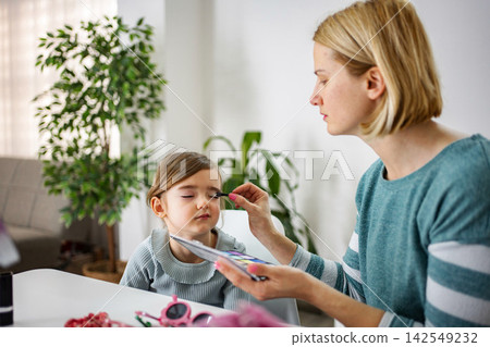 Mother applying eyeshadow to young daughter at home Mother applying eyeshadow to young daughter at home 142549232