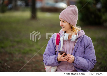 Young woman smiling holding smartphone wearing beanie headphones Young woman smiling holding smartphone wearing beanie headphones 142549259