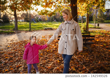 Mother and daughter holding hands walking in autumn park Mother and daughter holding hands walking in autumn park 142549326