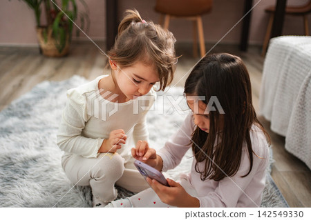 Young children focusing on screen playing mobile game together Young children focusing on screen playing mobile game together 142549330