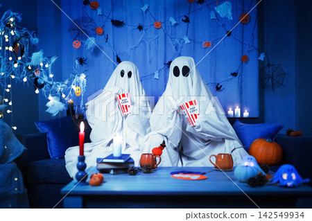 couple in ghost costume having Halloween fun at home. Spending a spooky night together, they hold popcorn, enjoying celebration, intimacy and entertainment. couple in ghost costume having Halloween fun at home. Spending a spooky night together, they hold popcorn, enjoying celebration, intimacy and entertainment. 142549934