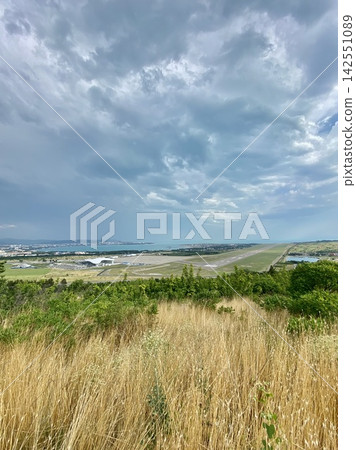 Airport runway stretches toward coastline beneath dramatic storm clouds in summer landscape. 142551089